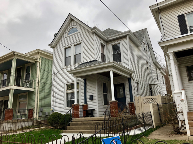 Reihe von Häusern mit Fenstern, Türen, Säulen, Geländern, Stufen und Dächern, umgeben von einem Metallzaun, Gras, Pflanzen und Bäumen unter einem bewölkten Himmel, mit einem Mietschild unten, das die Adresse als 5901 S Elmwood Ave, Chicago 60618 angibt.