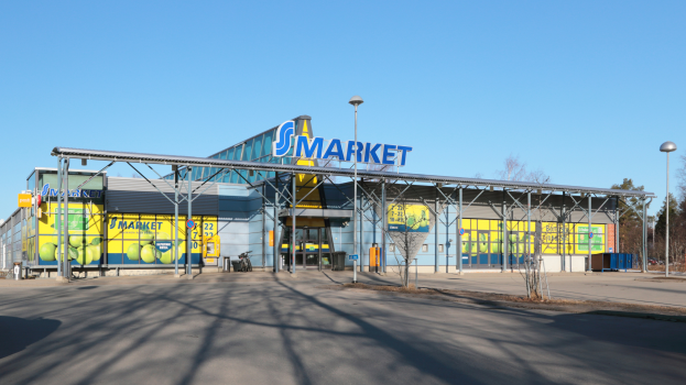 Ein große Gebäude mit einer "Smart Market"-Aufschrift, umgeben von Straßenmasten, Straßenlaternen, Kraftfahrzeugen, Bäumen und einem klaren blauen Himmel.