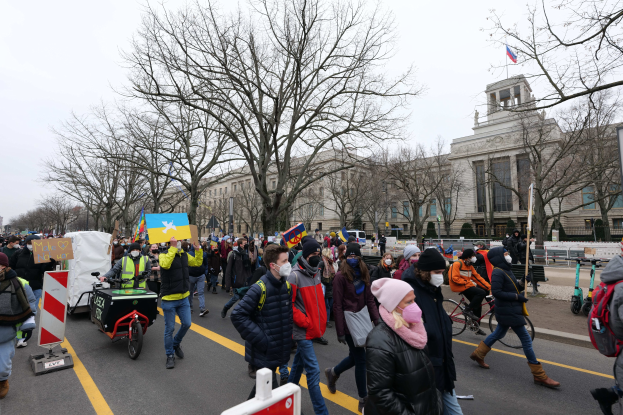 Eine große Gruppe von Menschen bei einer Protestdemo in Washington, D.C. am 21. Januar 2020, die eine Straße entlanggehen, Schilder, Banner und Fahrräder dabei, vor einem Gebäude mit Schildern, Bäumen und einem klaren blauen Himmel.