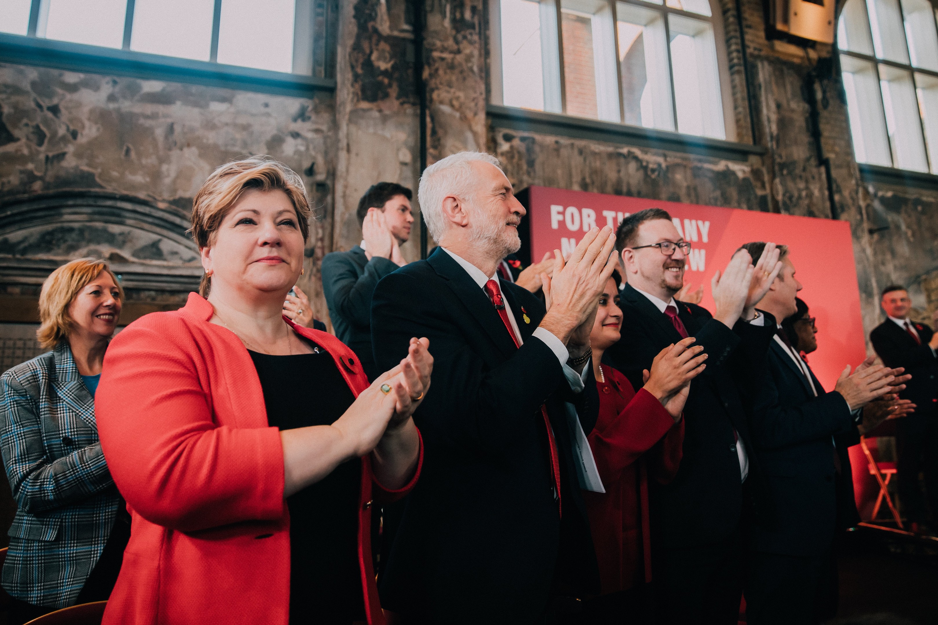 Eine Gruppe von Menschen, die vor einer Menge jubeln, mit einem Banner im Hintergrund, auf dem "Wahlsieg" steht