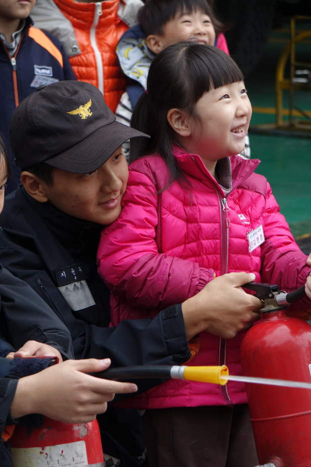 Gruppe von Kindern um ein rotes Feuerhydrant in einer Schulumgebung, mit einem Kind, das eine Leitung hält.