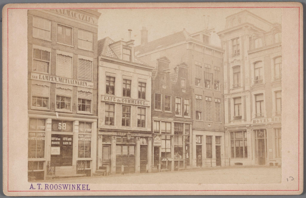 Altes Schwarz-Weiß-Foto einer Stadtstraße mit mehrstöckigen Gebäuden, die Fenster, Türen und Schilderbänder zeigen, mit schwachem Text unten.