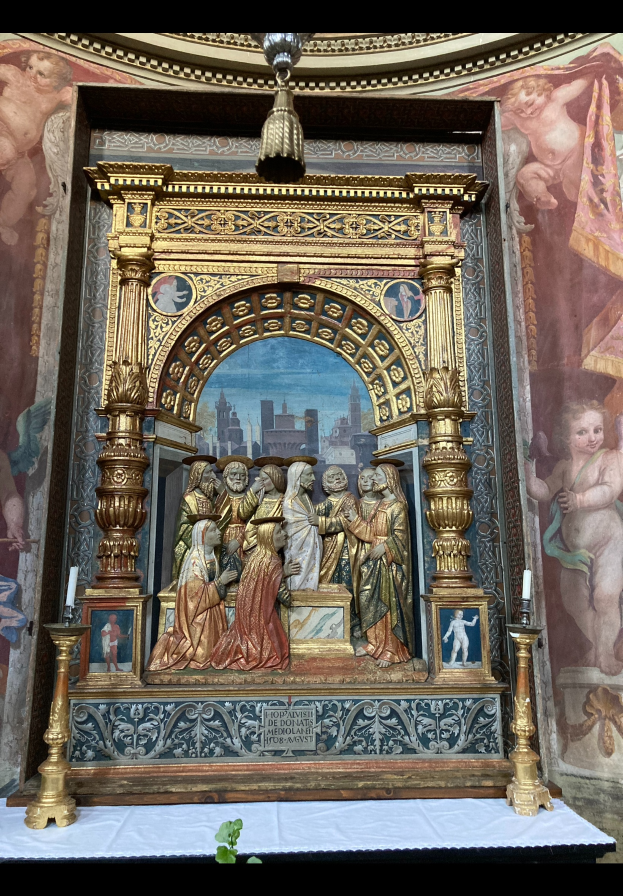 Ein Altar in einer Kirche mit Skulpturen, Kerzen und diversen Gegenständen vor einer Wand mit einem Gemälde und einer Pflanze unten für Grün