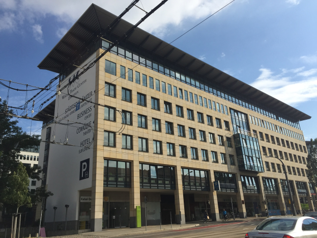 Großes modernes Gebäude mit vielen Fenstern, beschriftet als 'Stadthalle Center for Business', umgeben von Bäumen und städtischer Infrastruktur in Köln, Deutschland.