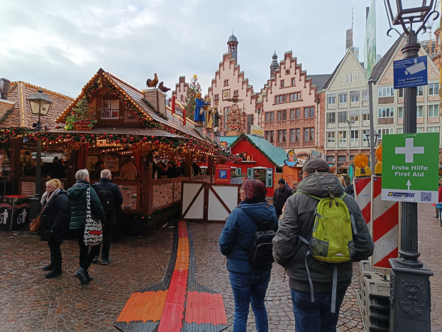 Menschen auf einem Kopfsteinpflasterweg neben einem Weihnachtsmarkt in Nürnberg, Deutschland, mit Laternenmasten, Informationsschildern und Gebäuden im Hintergrund.