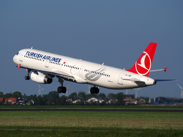 Turkish Airlines Airbus A330-300 startet von Frankfurt Airport, mit Gras darunter, Gebäuden und Bäumen im Hintergrund, Windmühlen in der Ferne und einem klaren blauen Himmel.