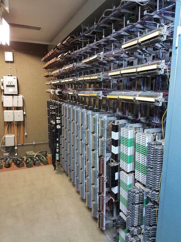 Ein unordentlicher Raum mit zahlreichen Servern, Kabeln und elektronischen Geräten auf dem Boden und einer Wand auf der linken Seite.