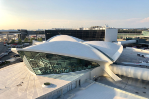 Luftaufnahme des neuen Terminalgebäudes am Los Angeles International Airport mit Fahrzeugen, Bäumen und Infrastruktur im Hintergrund bei bewölktem Himmel.
