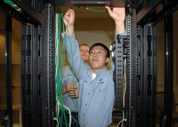 Zwei Männer arbeiten an einem Server in einem Rechenzentrum mit Gestellen voller Kabel und einer Wand im Hintergrund.