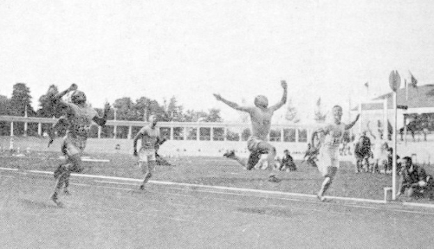 Schwarzes und weißes Foto von Männern, die auf einem Feld Fußball spielen, mit Zuschauern, Fahnen und Gebäuden im Hintergrund und dem Text "Sydney Football Club" unten.