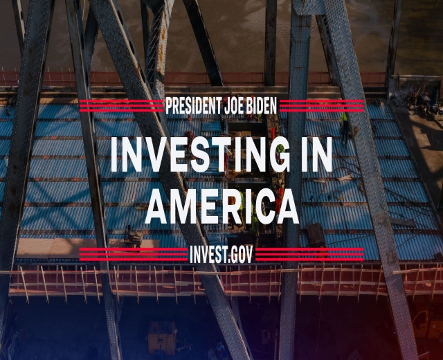 Präsident Joe Biden steht neben einer Brücke mit dem Text "Investing in America" im Vordergrund und verstreuten Gegenständen auf dem Boden.