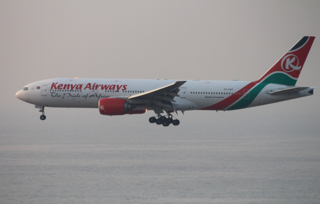 Airbus A330-300 von Kenya Airways im Flug mit weißer, roter und grüner Lackierung gegen einen blauen Himmel und glitzerndes Wasser darunter.