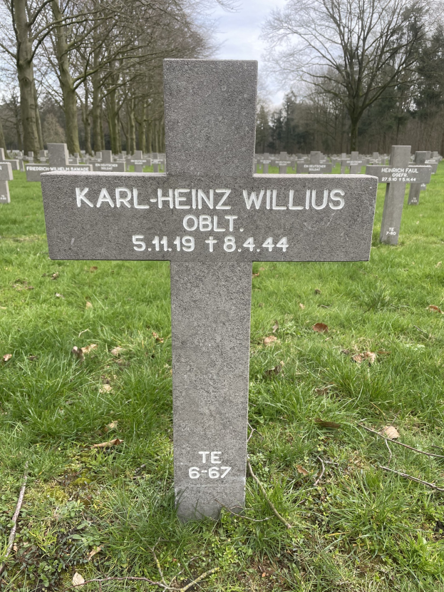 Grab von Karl-Heinz Willis auf einem deutschen Friedhof, umgeben von Gras und trockenen Bl├Ąttern mit Trees und einem klaren blauen Himmel im Hintergrund.