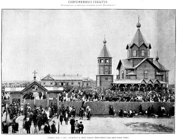 Schwarzes und weißes Foto einer Menschenmenge vor der Kirche der Interzession an der Nerl mit einem hölzernen Zaun im Vordergrund und Gebäuden im Hintergrund.