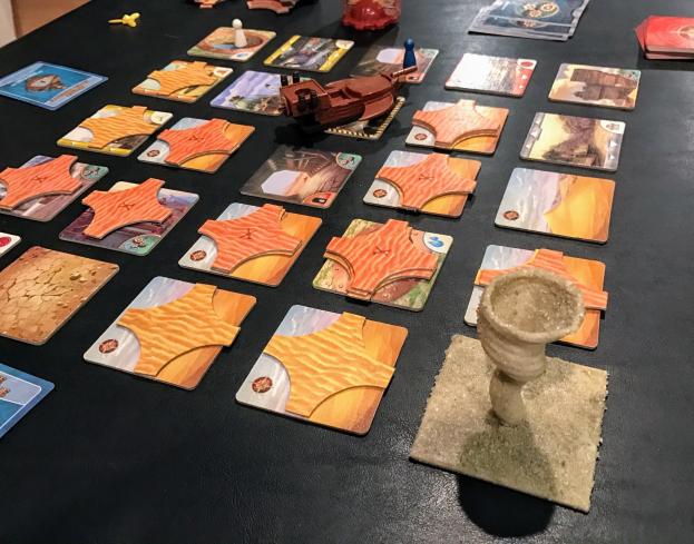 Ein Tisch voller Star Wars: The Old Republic-Brettspielkarten, Spielzeuge und andere Gegenstände in einem Raum mit einer sichtbaren Wand im Hintergrund.