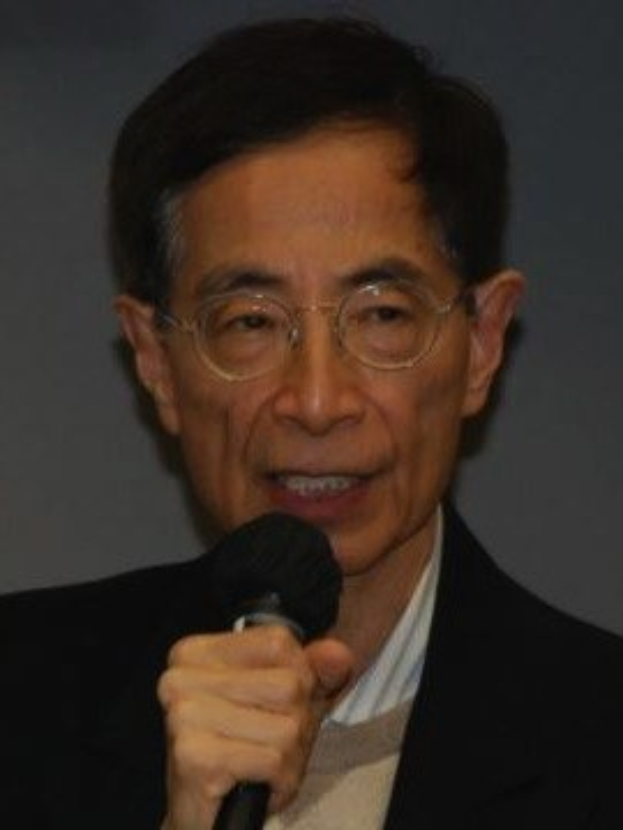 Ein ernst aussehender Mann in einem schwarzen Blazer und Brille hält ein Mikrofon, was darauf hindeutet, dass er Ökonom ist.