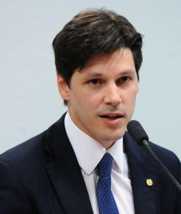 Ein Mann im Anzug und Krawatte spricht vor einer Wand in ein Mikrofon und scheint eine Regierungsentscheidung zu kommentieren.