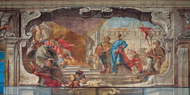 Ein lebendiges Fresko an einer Decke, das eine vielfältige Gruppe von realistisch gestalteten Menschen zeigt, einige in traditioneller und andere in moderner Kleidung, umgeben von Skulpturen und verschiedenen Gegenständen, die eine lebendige Szene schaffen.