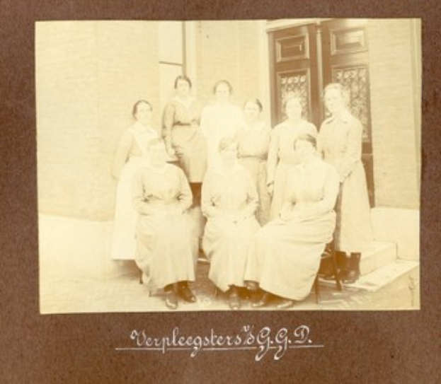 Schwarz-weißes Foto einer Gruppe von Frauen, die auf Außentreppen vor einem Gebäude mit einer Wand und einer Tür sitzen; verblichener Text erscheint unten.