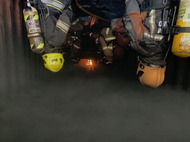 Feuerwehrleute mit Helmen und Jacken mit Atemschutz arbeiten in einem raucherfüllten Tunnel, der von einem entfernten Licht beleuchtet wird.