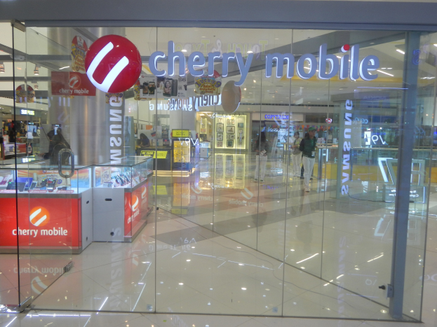 Cherry Mobile-Ladeninneres in einem Einkaufszentrum mit Glaswänden und Deckenbeleuchtung, Menschen, die gehen, und Auslagentischen mit Gegenständen.
