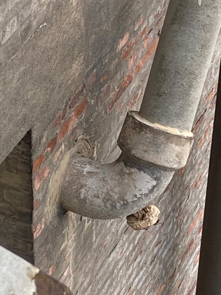 Nahaufnahme eines Metallrohrs an einer Gebäudefassade mit Reparaturwerkzeugen und Materialien drumherum.