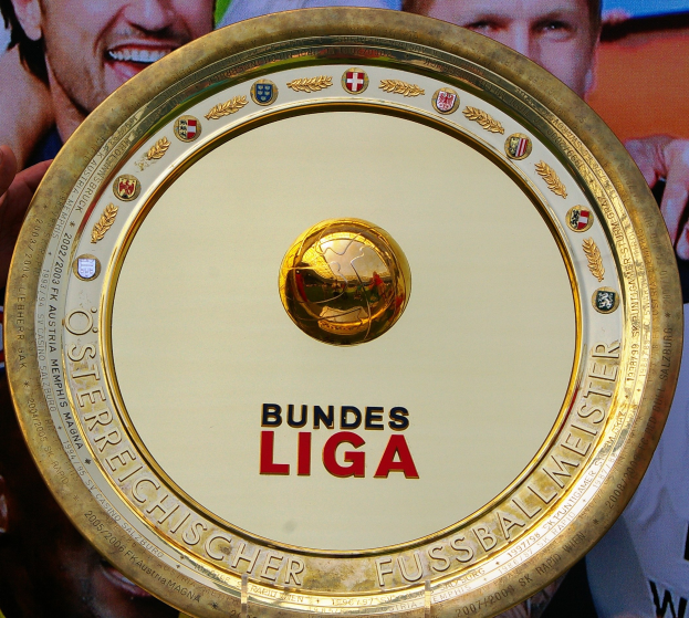 Goldener Schild mit 'Bundesliga'-Text in der Hand eines Mannes, mit einem Banner mit drei Personen im Hintergrund.