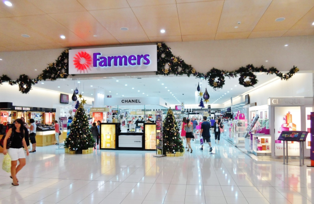 Menschen gehen durch ein Weihnachtsdekorationen Einkaufszentrum mit beleuchteten Bäumen, festlichen Auslagen und einer Deckenmontage mit Text, einige tragen Einkaufstaschen.