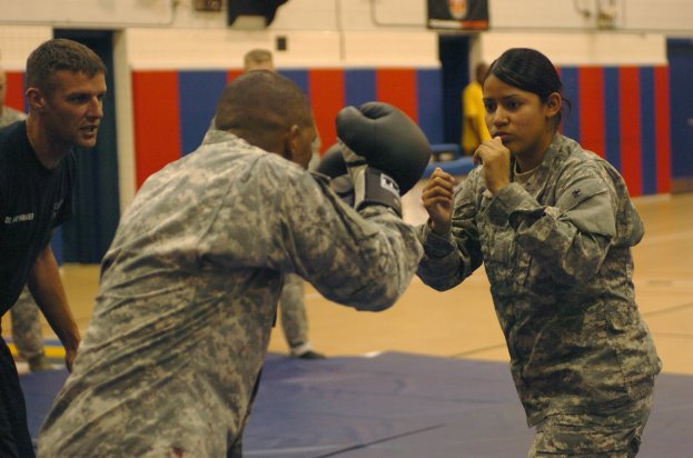 Gruppe von Menschen in Militärkleidung beim Sparring in einem Fitnessstudio mit einer Wand im Hintergrund, die Handschuhe tragen und in einem Match gegeneinander antreten.