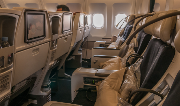 Eine Reihe leerer Business-Class-Flugzeugsitze mit einer Person an Bord, Fenster auf der rechten Seite mit Außenansicht.