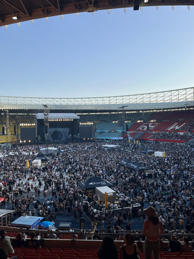 Große Zuschauermenge auf Tribünen und Stehplätzen in einem Stadion mit Geländern, Zelten und Überdachung, mit dem Himmel im Hintergrund.