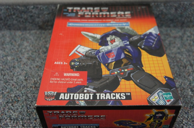 Ein roter, oranger und blauer Autobot Tracks-Roboterkasten mit schwarzem unscharfen Hintergrund.