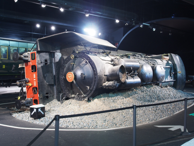 Eine alte Dampflokomotive in einem Museum ausgestellt, umgeben von Steinen und beleuchtet von Deckenlampen.