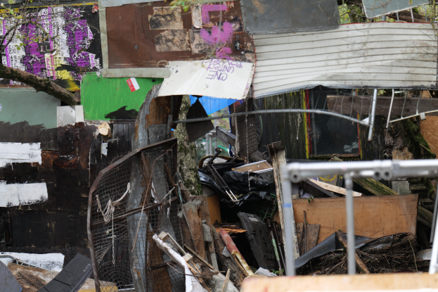 Ein Haufen Müll liegt vor einem mit Graffiti beschmierten Gebäude, umgeben von Bäumen und anderen Gegenständen.