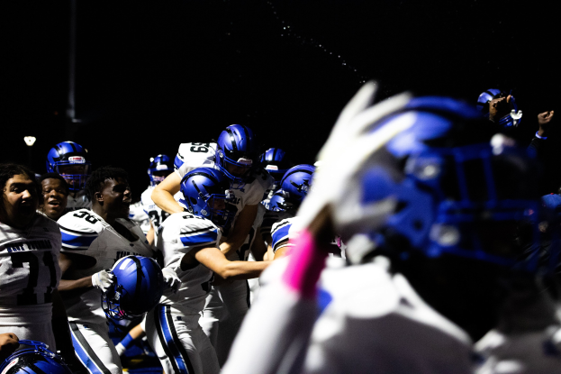 Eine Gruppe von Fußballspielern in weißen Uniformen und blauen Helmen auf einem dunklen Feld bei Nacht zusammengedrängt.