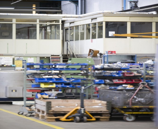 Großes Lagerinneres mit verschiedenen Geräten einschließlich fahrbaren Wagen, Schränken und einer Box, mit einer Glasfensterwand und freiliegenden Rohren im Hintergrund.