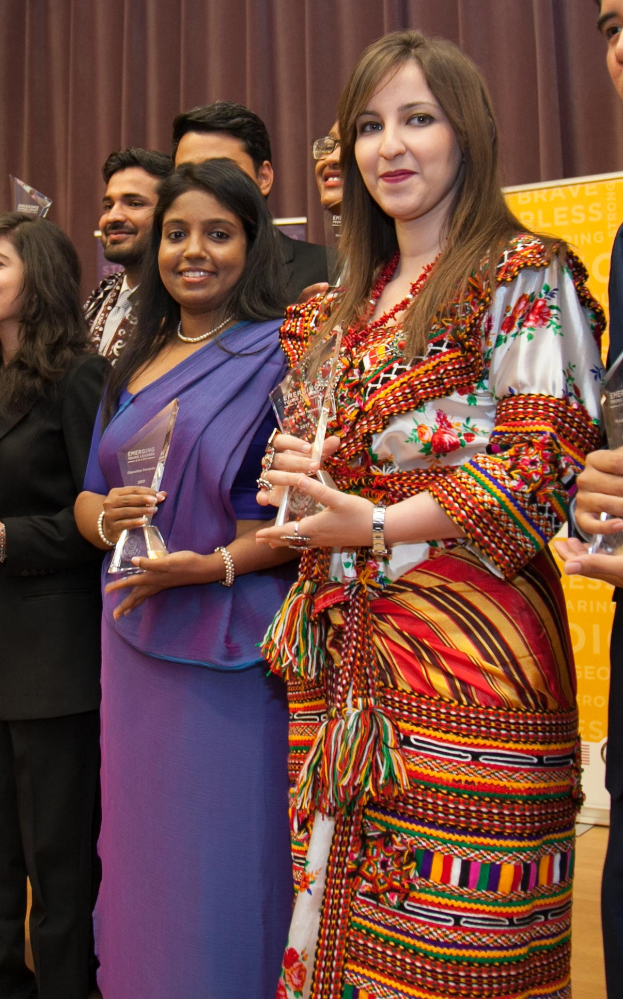 Eine Gruppe von Menschen auf einer Bühne mit einer Frau in der Mitte, die einen Pokal hält, hinter einem Vorhang mit einer Tafel, auf der "Bravo Segenspreis-Gewinner" steht.