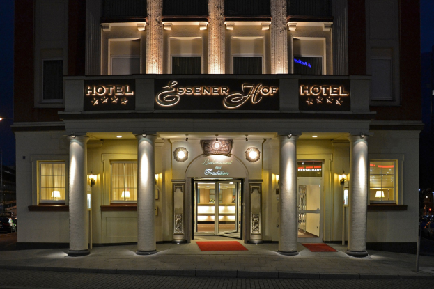 Das Essenerhof Hotel in Berlin, Deutschland, ein mehrstöckiges Gebäude mit Fenstern, Türen, Säulen, Lampen und einem Namensschild, mit einer Straße und Fahrzeugen auf der rechten Seite, unter einem klaren Himmel.