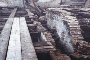Altes Gebäude in Abbruch mit verstreuten Holzplanken und Steinen auf dem Boden und einer Wand im Hintergrund.