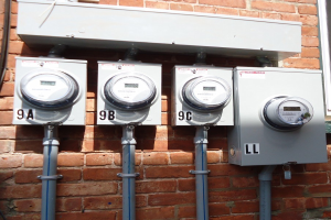 Drei Stromzähler an der Seite eines Backsteingebäudes montiert, verbunden mit Rohren, mit einem Fenster auf der rechten Seite.