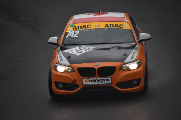 Ein oranges BMW-Rennfahrzeug mit Text und Zahlen auf der Karosserie fährt auf einer Rennstrecke.