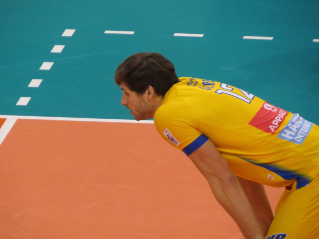 Eine professionelle Volleyballspielerin in einem gelben T-Shirt steht selbstbewusst auf einem Feld und ist bereit, den Ball zu servieren.