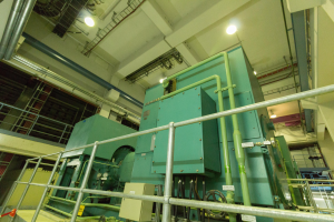 Ein großes industrielles Wärmetauschergerät in einem Gebäude umgeben von Geländern, Rohren, Lampen und anderer Ausrüstung.