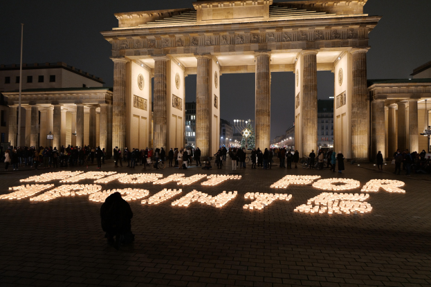 Eine Gruppe von Menschen steht vor dem beleuchteten Reichstagsgebäude in Berlin, Deutschland, umgeben von Gebäuden, Pfählen und Lichtern, und die Wörter 'Kampf für die Freiheit' sind auf den Boden geschrieben.