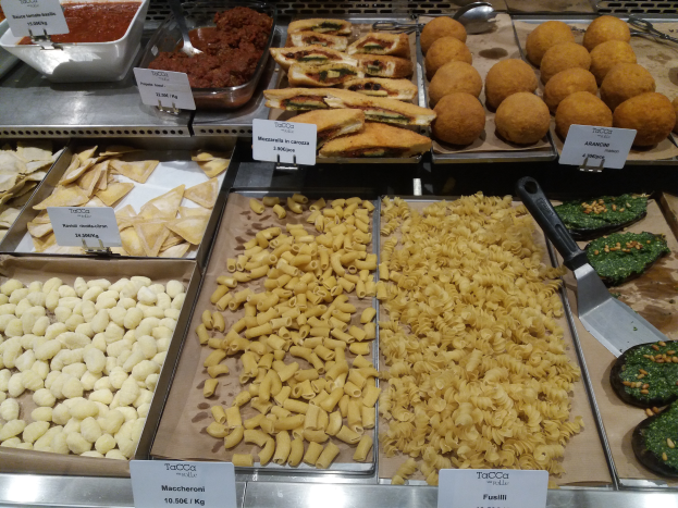 Ein Schaukasten voller verschiedener italienischer Lebensmittel, darunter Schalen und Schüsseln mit verschiedenen Pastasorten, mit Schildern, die die Lebensmittelarten angeben.