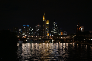 Die Frankfurter Skyline bei Nacht, mit beleuchteten Gebäuden und Sternen im Wasser gespiegelt.