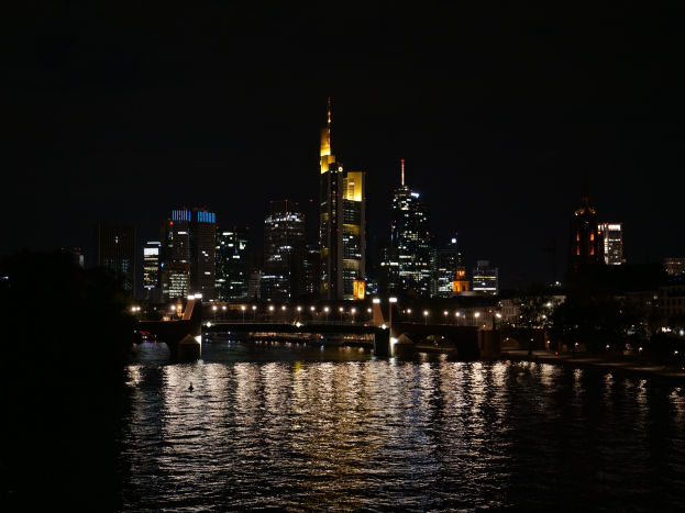 Die Frankfurter Skyline bei Nacht, mit beleuchteten Gebäuden und Sternen im Wasser gespiegelt.