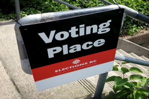 Ein Wahlplatz-Schild an einem Gebäude mit einer Tafel, die an einem Geländer befestigt ist und Pflanzen im Hintergrund.