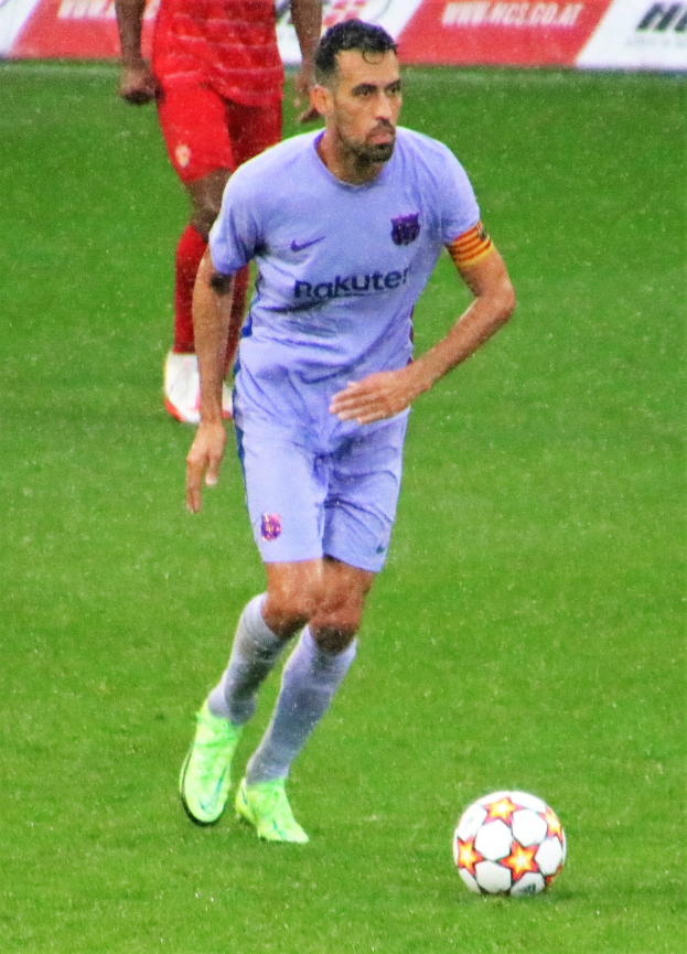 Ein Fußballspieler in Sportkleidung und Stollenschuhen auf einem Feld mit einer Texttafel im Hintergrund.