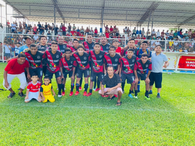 Gruppe von Männern auf einem Fußballfeld mit einem Siegesschild 'Fotos Ugarte U-17 vs U-18' unter einem bewölkten Himmel.